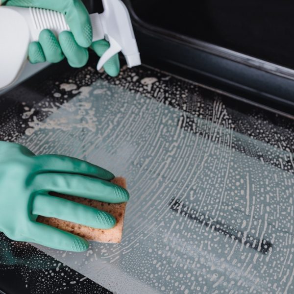 Woman,In,Green,Gloves,Cleaning,Oven,Door,With,Sponge,In
